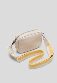 Beige keinoksyntheettinen crossbody-laukku, jossa on vetoketjukiinnitys ja irrotettava keltavalkoraitainen hihna. Sujuva pinta ja suorakulmainen muoto.