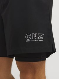 Pantalones cortos deportivos negros con cintura ajustable, que presentan un logo de marca en blanco "CNZ™ CORE NINE.ZERO" en la pierna izquierda. Textura suave.