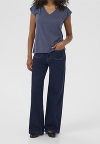 Marinblå V-ringad t-shirt med korta ärmar, tillsammans med mörkblå utsvängda jeans. Slät yta och klassisk denimdesign med fickor.