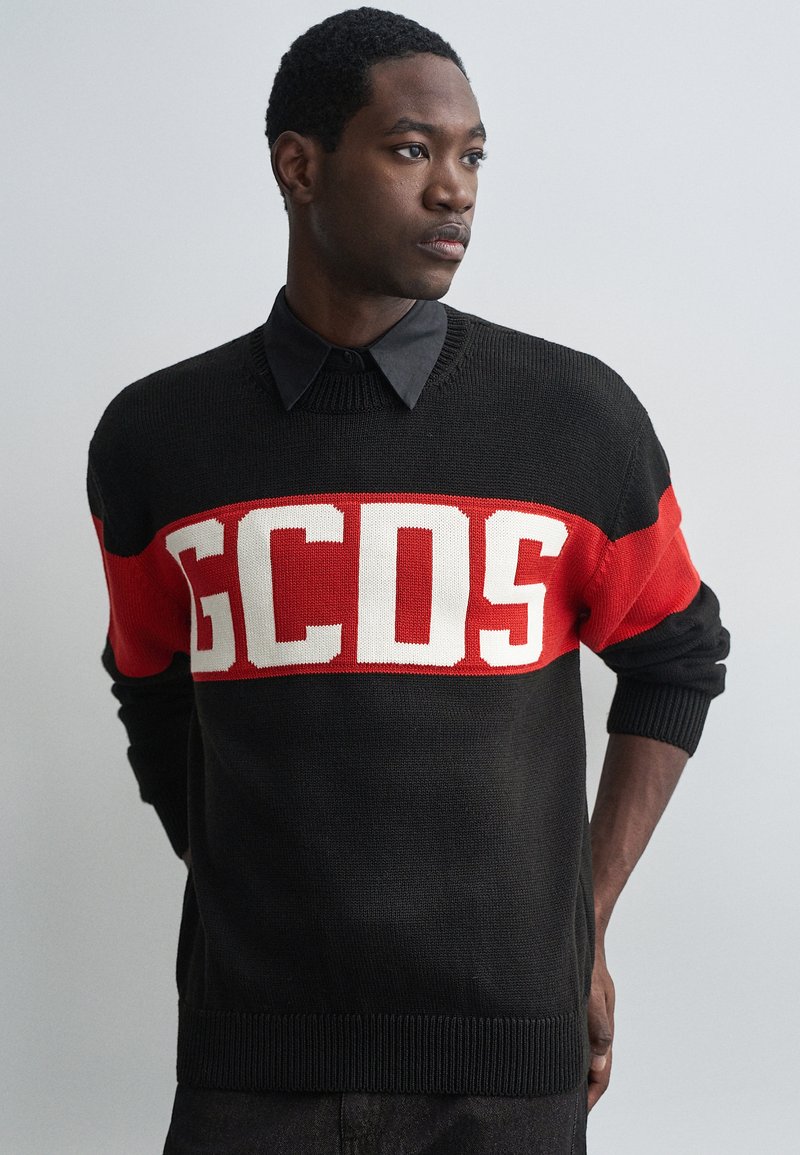 Pulôver tricotado em preto e vermelho com grande texto branco "GCDS", gola e punhos canelados, com riscas horizontais em contraste.