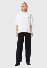 Άσπρο oversized μπλουζάκι με κοντά μανίκια, διακοσμημένο με μαύρο λογότυπο. Συνδυασμένο με μαύρα τζιν φαρδιάς γραμμής και μαύρα μποτάκια αστραγάλου.