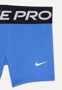 Shorts de sport bleus avec une taille noire portant le texte "NIKE PRO" et un logo Nike blanc sur le côté. Fabriqués en tissu lisse et extensible.