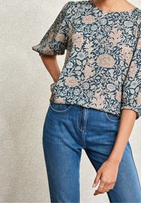 Top con motivo floreale in tonalità navy e rosa pallido, caratterizzato da un collo rotondo e maniche corte. Abbinato a jeans di denim blu classici.