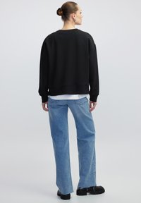 Zwarte sweatshirt met een relaxed fit, geribde manchetten en onderrand, gedragen over een witte shirt, in combinatie met lichtblauwe recht gesneden jeans.