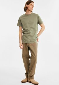 Oliven grøn bomuld t-shirt med rund hals, parret med beige cargo-bukser med synlige sømme og sidelommer. Afsluttet med brune sko.