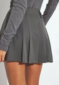 Falda plisada en tela gris oscuro, con una cinturilla alta y una textura suave. Detalle de cremallera expuesta en la parte posterior.