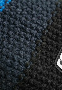 Textured fabric in dark blue and black hues, featuring a woven pattern with a soft finish. An attached rectangular label in white.