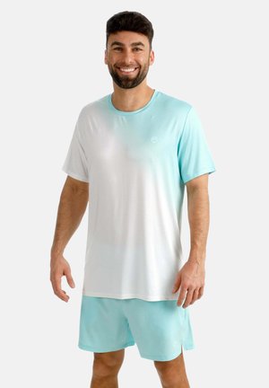 Lächelnder Mann trägt ein hellblau-weißes Gradient-T-Shirt mit passenden hellblauen Shorts, steht vor einem schlichten Hintergrund.