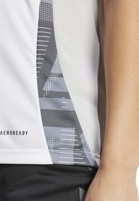 Maglietta atletica bianca con motivo geometrico grigio e dettagli testurizzati sui lati. Realizzata in tessuto traspirante e con logo "AEROREADY".