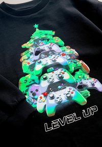 Schwarzer Pullover mit einem lebhaften Grafikdesign von übereinander gestapelten Spielcontrollern, die einem Weihnachtsbaum ähneln, gekrönt von einem Stern und bunten Akzenten.