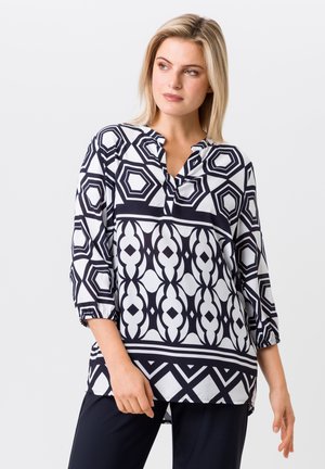 Tunique noire et blanche avec des motifs géométriques, dotée d'un col rond, de manches 3/4 et d'une coupe légèrement décontractée. Texture de tissu lisse.