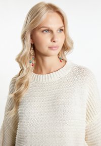 Pulover crem tricotat cu guler rib sută, având un model texturat. Cercei aurii cu mărgele colorate și accente în formă de lacrimă.