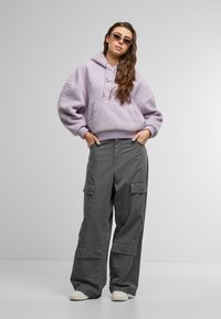 Lavendel fleece hoodie met een kangoeroezak, gecombineerd met grijze cargobroek met meerdere zakken en witte sneakers.