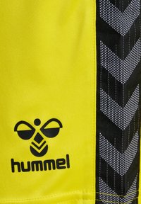 Helle gelbe Stoffshorts mit einem schwarz-weißen Fischgrätenmuster an der Seite und einem auffälligen schwarzen "hummel"-Logo.