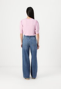 Light pink short-sleeve sweater with puffed sleeves paired with high-waisted, wide-leg blue denim jeans. Simple design and soft texture.