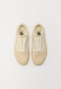 Beige mockalädersneakers med vit lädersidostråk och vita snören. Har en rund tå och en texturerad gummisula.