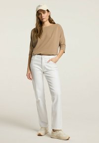 Beżowa koszula z długim rękawem, białe dżinsy z prostymi nogawkami i kremowe sneakersy. Koszula ma luźny krój; dżinsy mają kieszenie z przodu.