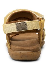 Keltaiset sandaalit, joissa on pehmeä ruskea mokkanahkainen pohja, tekstiiliremmit ja teksturoitu beige accentti. Varusteena metalliosat ja joustava pohja.