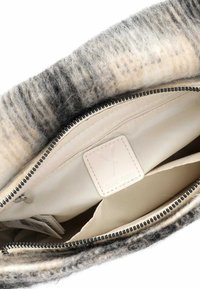 Interno di una borsa in lana grigia e beige, con una fodera in tessuto liscio, dotata di una cerniera nera e scomparti di stoccaggio separati. Etichetta in pelle con logo visibile.