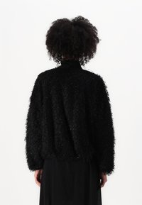 Cardigan negru texturat, realizat dintr-un material pufos, cu o croială liberă și guler înalt. Designul are un aspect moale și zbârlit.