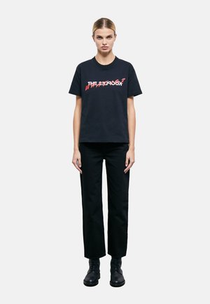 Camiseta de algodón negra con texto gráfico rojo, combinada con pantalones rectos negros y botas negras con cordones. Diseño simple y casual.