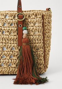 Geflochtene Strohtasche mit einem hellbraunen Ledertragegurt, runder Messingbeschläge und einem mehrfarbigen Quasten, gefertigt aus verschiedenen Texturen und Fasern.