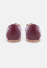 Burgundy leather flats with a rounded back, minimalistic design, and a light-colored, textured sole. No visible embellishments.