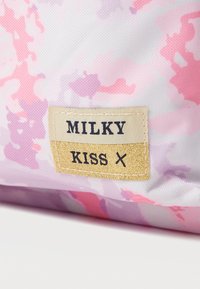 Tyg med rosa och lila kamuflagemönster med en sydd beige och guld etikett som står "MILKY KISS X."