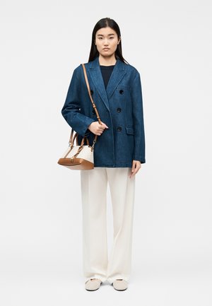 Žena v tmavě modrém dvouřadém saku, bílých širokých kalhotách, béžových botách a s béžovo-hnědou kabelkou s ramenním popruhem.