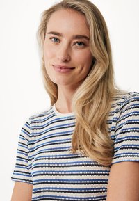 Pruhovaný pletený top s horizontálními vzory v modré, bílé a černé barvě, krátké rukávy a kulatý výstřih. Měkká textura a přiléhavý střih.