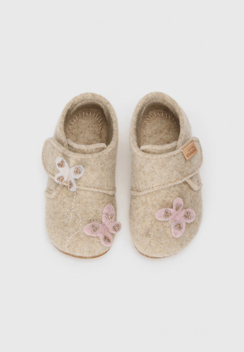 Chaussons en feutre beiges avec une bride à velcro. Agrémentés d'appliqués en forme de papillon blancs et roses et de légers détails de couture.