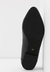 Sole di scarpa in pelle nera con forma appuntita. Caratterizzata da una superficie testurizzata e dalla taglia "37" in rilievo dorato. Design piatto, con dettagli minimi.