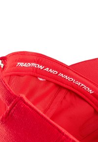 Czerwona czapka z teksturowanej tkaniny. Wewnątrz znajduje się biały napis "TRADYCJA I INNOWACJA". Prosty design z zaokrąglonymi krawędziami.