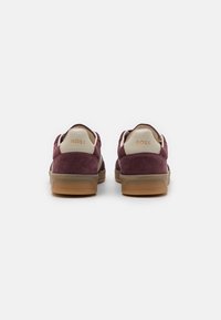 Sneakers in deep burgundy suede with tan accents and a light-colored heel. Features a textured sole and embossed logo on the back.