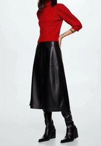 Pull à col roulé en tricot rouge avec des manches bouffantes, associé à une jupe droite en cuir noir et des bottes à plateforme noires montantes.