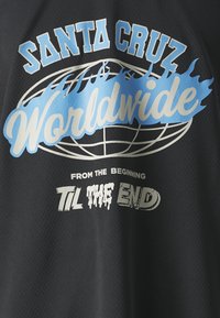 Camiseta de tela de malla negra con texto en blanco y azul claro. El texto incluye "SANTA CRUZ Worldwide" y "DESDE EL PRINCIPIO HASTA EL FINAL."