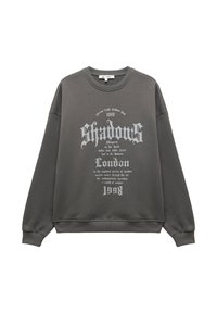 Ciemnoszary sweatshirt z okrągłym dekoltem, z białym tekstem w stylu gotyckim, który głosi "Shadows London 1998", oraz dodatkowym mniejszym tekstem dekoracyjnym.