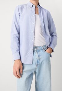 Lichtblauw katoenen overhemd met knopen en een kraag, gedragen over een wit tanktopje. Gecombineerd met lichtblauwe spijkerbroek. Eenvoudig ontwerp, casual pasvorm.