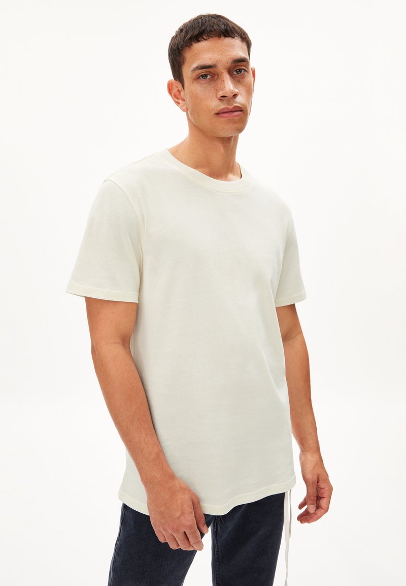 T-shirt en coton beige clair avec un col rond et des manches courtes. Le tissu semble doux, présentant un design uni sans motifs visibles.