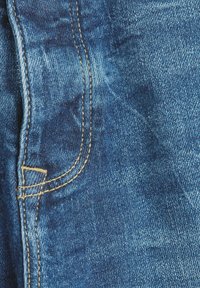 Lähellä denim-kangasta, jossa on syvä sininen väri, näkyvät kontrastiset kultaiset langat ja kevyet tekstuurivaihtelut.