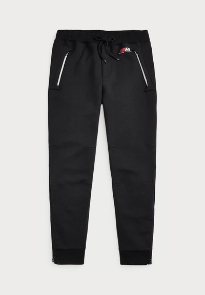 Pantalon de survêtement noir avec une taille à cordon de serrage, deux poches latérales zippées, des poignets côtelés et un petit logo à l'avant.