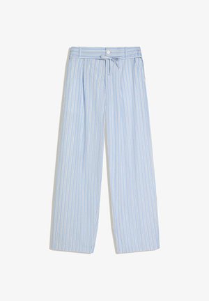 Homme portant un pantalon ample à rayures verticales bleu clair et blanc avec un cordon, des chaussures noires, une chemise foncée et un haut beige à l’intérieur.