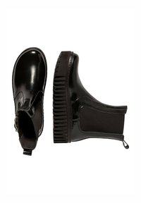 Botas Chelsea negras con un acabado brillante, paneles laterales elásticos y suela de goma estriada. Cuenta con una lengüeta en la parte trasera para facilitar el uso.