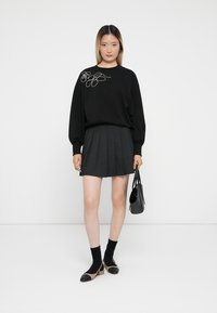 Svart sweatshirt med blomsterbroderi, sammen med en plisséskjørt i mørkegrå. Svart sokker og to-tonet sko i svart og beige. Liten svart håndveske.