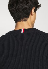 Pull en maille marine foncé avec une texture côtelée, col rond orné d'un accent rouge, blanc et bleu à l'arrière.