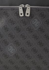 Juodas tekstūruotas audinys su deimanto raštu, kuriame yra logotipas. Sidabrinės užtrauktuko detalės su dviem trauklėmis, papildančiomis funkcionalumą ir dizainą.