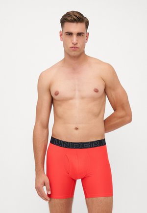 Herren-Boxershorts in leuchtendem Rot, mit einem schwarzen elastischen Bund, der das "UNDER ARMOUR"-Logo trägt, und aus glattem, enganliegendem Material gefertigt.