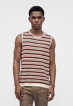 Homme portant un haut sans manches en maille avec des rayures horizontales blanches, orange, noires et marron, debout devant un fond clair uni.