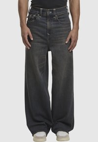 Ciemnoniebieskie dżinsy o szerokich nogawkach z wysokim stanem, pięcioma kieszeniami i subtelnym wyblaknięciem. W zestawieniu z białymi i szarymi sneakersami.