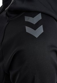 Zwart sportkledingstuk met een gladde textuur; heeft twee grijze chevron-accenten aan de zijkant, die de zichtbaarheid en het ontwerp verbeteren.